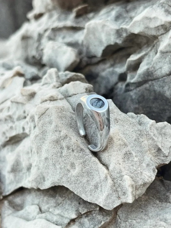 Silver signet ring with Picasso dolomite on natural rock background.